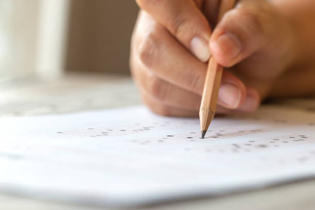 istock Exam test school or university concept : Hand student holding pencil writing standardized answer multiple carbon paper form with gray black answers sheet bubbled of question in examination assessment. 1153649303