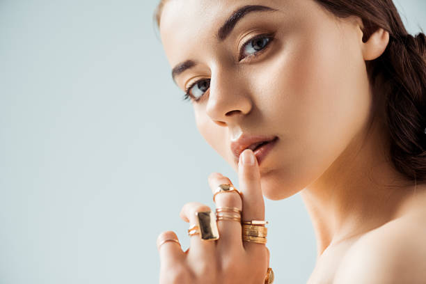 jeune femme avec le maquillage brillant et les anneaux dorés touchant les lèvres d’isolement sur le gris - jewelry photos et images de collection