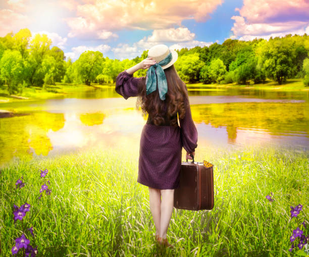 폴카 도트 드레스와 모자에 곱슬 머리를 가진 젊은 여자는 호수 쇼 어에 서 있는 복고풍 스타일의 가방과 일몰 전에 구름과 멋진 하늘을 보고 - polka dot suitcase retro revival women 뉴스 사진 이미지