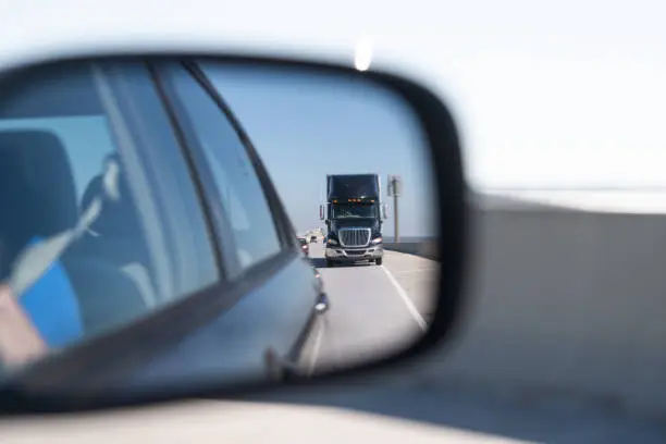 Car window side mirror on sunny day with truck traffic in reflection in Florida transporation highway street road
