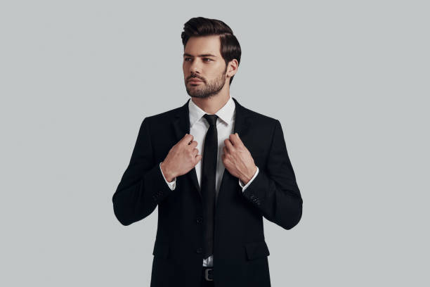 istock Confident in his style. Handsome young man in full suit adjusting jacket and looking away while standing against grey background 1153665458