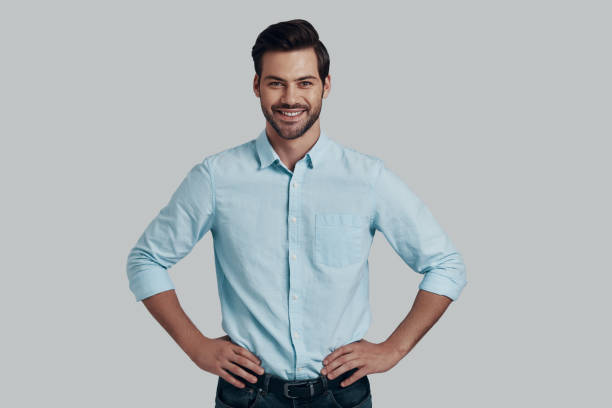 istock Feeling confident. Handsome young man looking at camera and smiling while standing against grey background 1153665803