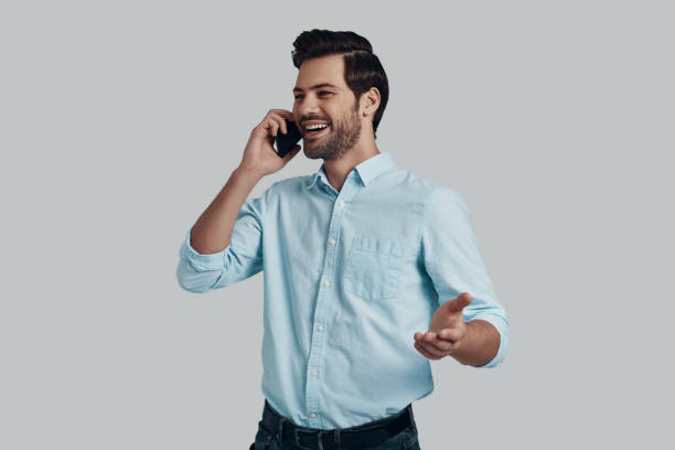 istock Good talk. Handsome young man talking on the phone and smiling while standing against grey background 1153666019