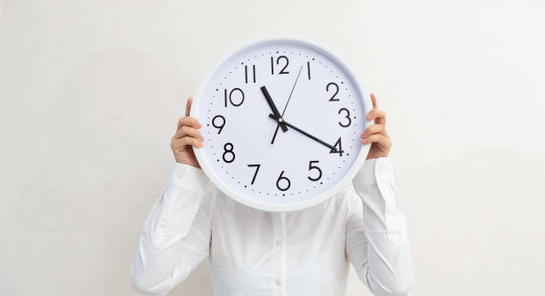 istock Businesswoman holding a clock against wall 1153666389