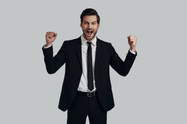 istock I did it! Handsome young man in full suit gesturing and shouting while standing against grey background 1153666441