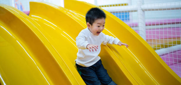 Little boy sliding down from the yellow slide, laughing