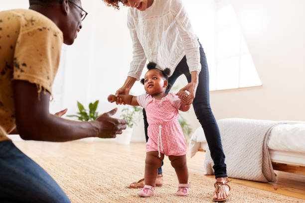 istock Parents At Home Encouraging Baby Daughter To Take First Steps 1153667574