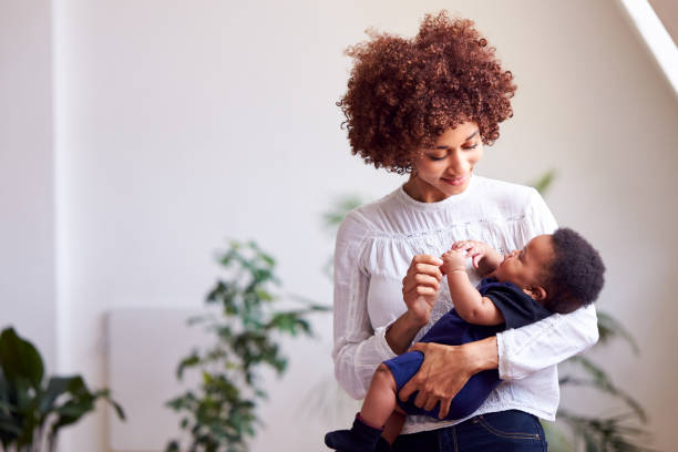 ロフトアパートメントで自宅で生まれたばかりの赤ちゃんを抱いて愛する母親 - baby mother newborn african descent ストックフォトと画像