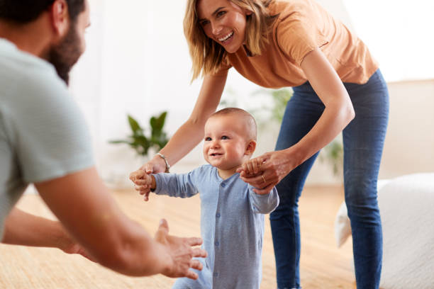 parents à la maison encourageant le fils de bébé à prendre les premiers pas - baby walking child standing photos et images de collection