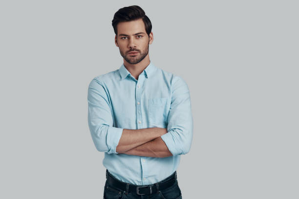 istock Perfect in every way. Handsome young man looking at camera and keeping arms crossed while standing against grey background 1153667875