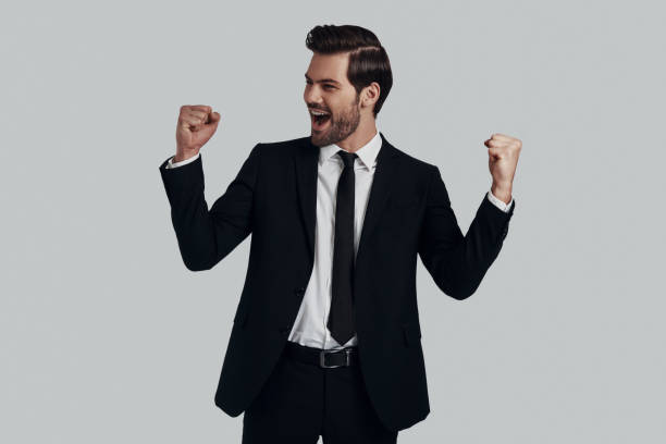 istock Success! Handsome young man in full suit gesturing and shouting while standing against grey background 1153668989