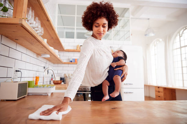 istock Multi-Tasking Mother Holds Sleeping Baby Son And Cleans In Kitchen 1153669132