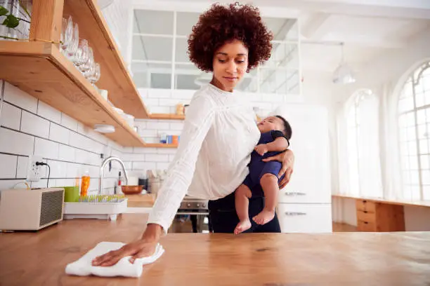 Photo of Multi-Tasking Mother Holds Sleeping Baby Son And Cleans In Kitchen