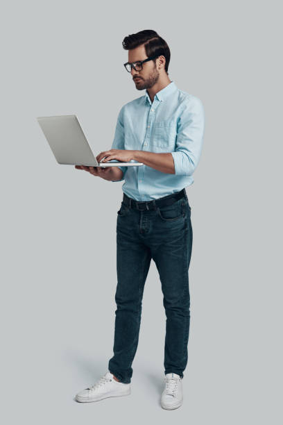 istock Surfing the net. Full length of young man using laptop while standing against grey background 1153669140