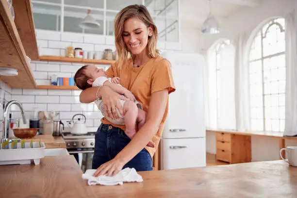 Photo of Multi-Tasking Mother Holds Sleeping Baby Son And Cleans In Kitchen