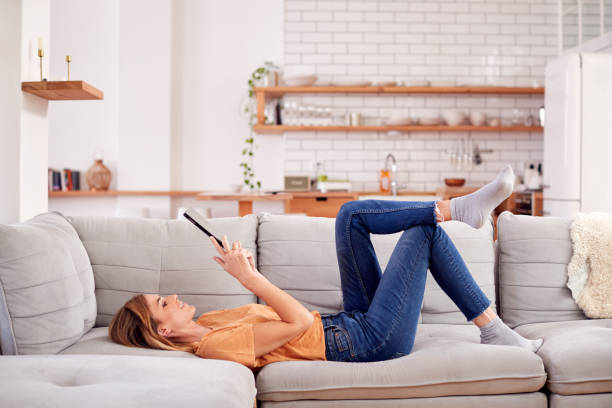 женщина расслабляющий лежа на диване дома глядя на цифровой планшет - ipad television digital tablet connection стоковые фото и изображения
