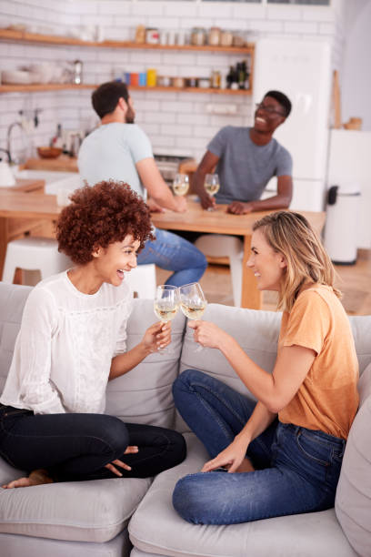 istock Two Couples Relaxing On Sofa At Home With Glass Of Wine Talking Together 1153669902