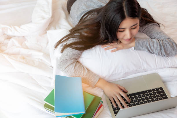 istock Beautiful university student searching information on internet online by using laptop computer at cozy bedroom after go back home from university. Attractive teenager woman feel happy with smile 1153670968