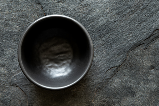 Black empty ceramic bowl isolated on dark grey slate from above. Space for text.