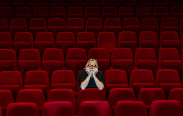 istock One man with white beard sits in Empty cinema or theatre with comfortable red seats 1153676808
