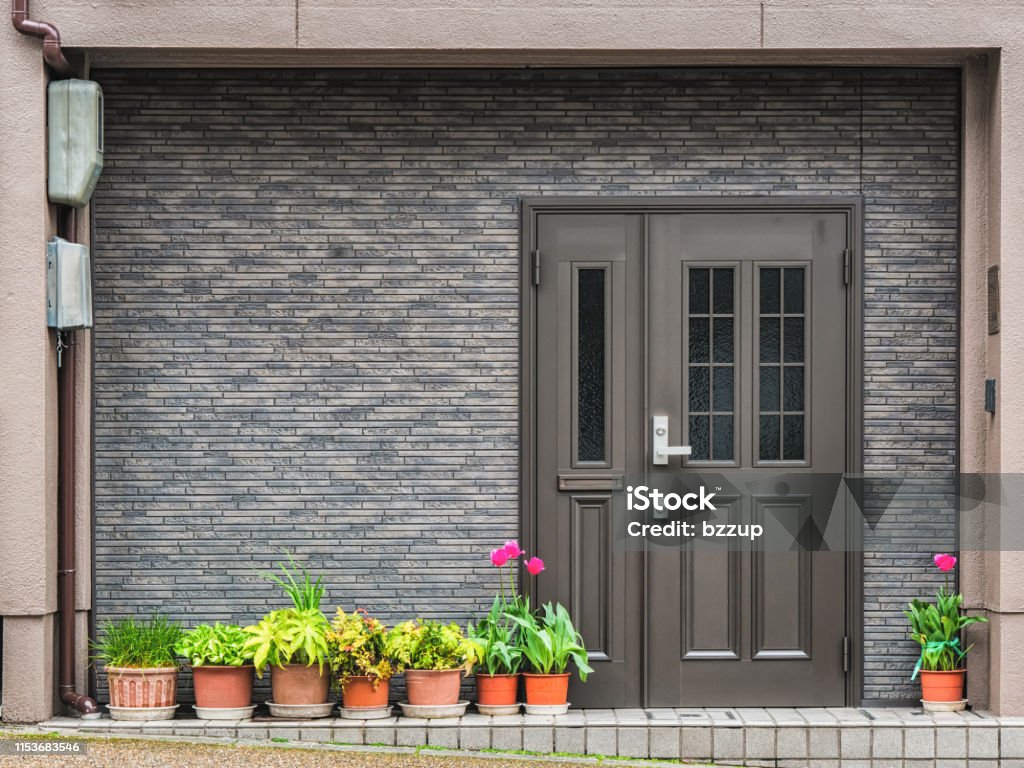 Gray front door with small square decorative windows and flower pots in fron of it Gray front door with small square decorative windows and tiled concrete wall with flower pots in fron of it Front Door Stock Photo