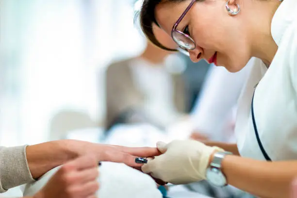 Manicurist using a cuticle trimmer tool to remove excess skin off a fingernail in a beauty cosmetic center.