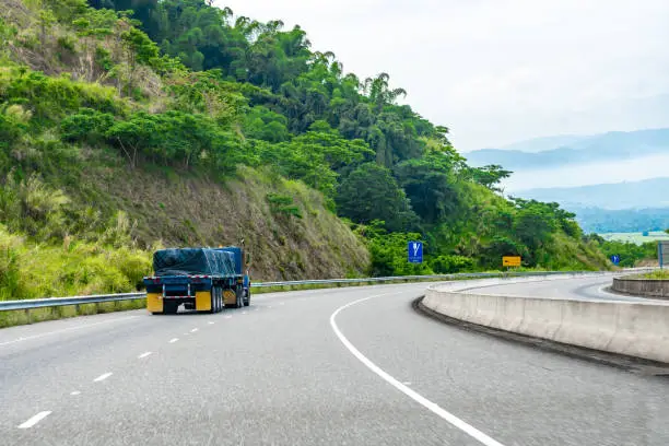 Photo of Loaded 22 wheeler cargo semi trailer truck covered and tied/strapped down with rope driving on left hand side of road on dual carriageway.