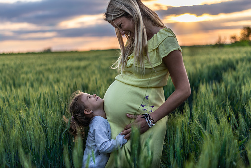 Young pregnant mother spending time with her daughter in nature on a sunset.