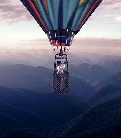 Man looks through binoculars flying with hot air balloon above mountains.
