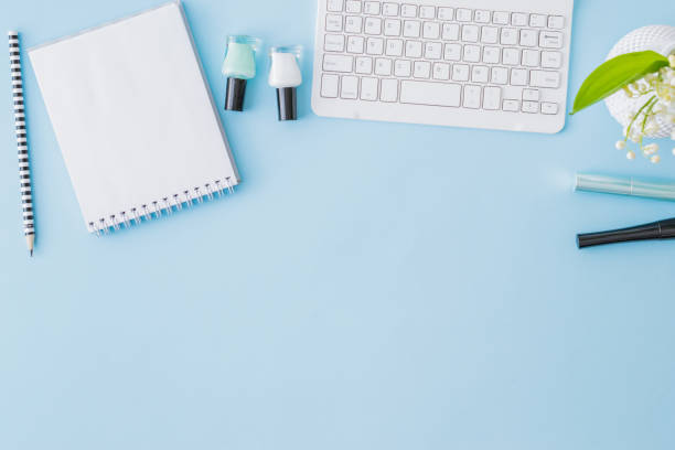 istock Flat lay blogger or freelancer workspace with a notebook, keyboard and lily of the valley flowers on a blue background 1153687327