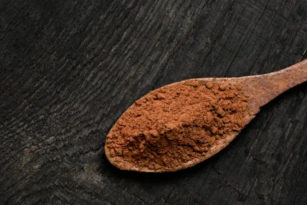 Cocoa powder on a wooden spoon isolated on black rustic wood board from above. Space for text.