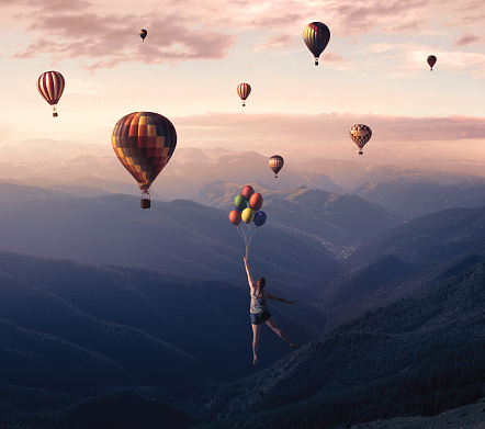La joven salta del acantilado de la montaña y vuela con globos de aire caliente. photo