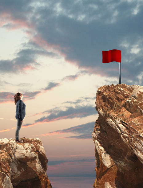 istock Woman looking to a red flag over a gap between two mountain peaks. 1153687853