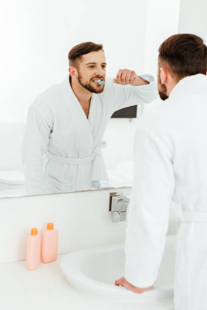 istock selective focus of handsome man brushing teeth while looking at mirror in bathroom 1153687998