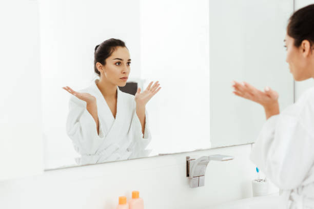 istock selective focus of attractive brunette woman gesturing while looking at mirror in bathroom 1153688520