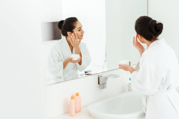 istock selective focus of attractive woman applying face cream while looking at mirror 1153688549