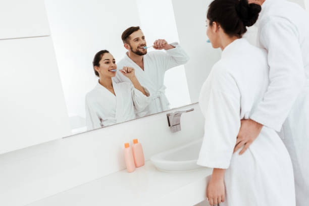 istock cheerful couple looking at mirror and brushing teeth while standing in bathrobes 1153688696
