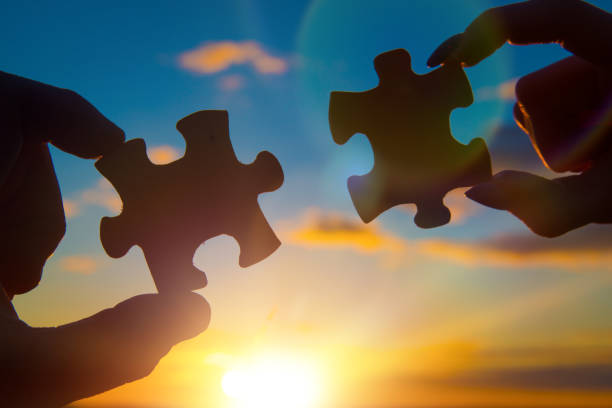 istock Two hands assemble a puzzle into one. On the background of the sunset. 1153689084