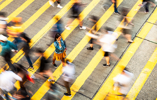 Motion blur as people cross the street at a zebra crossing, while a woman slowly walks, as she talks on the phone.