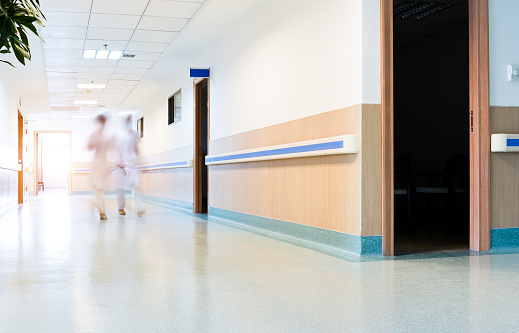 Blurred figures wearing medical uniforms walking through the hallway in hospital
