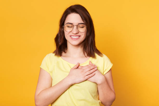 istock Image of charming woman keeps hands together on chest, expresses gratitude, keeps eyes closed, makes thankful gesture, thanks God for something pleasant. Body language, human emotions concept. 1153696809