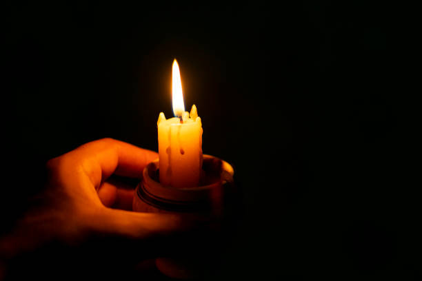 istock burning wax candle in hand on black background 1153697727