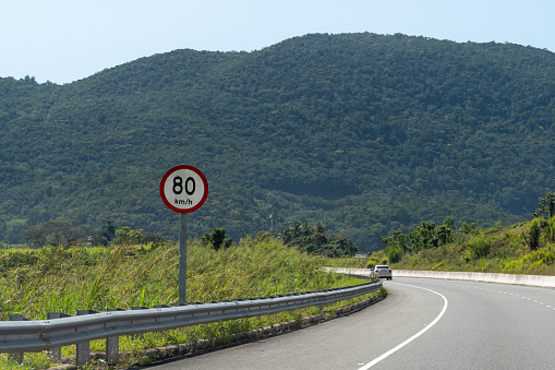 80 km/h circular/round red and white speed limit street traffic sign on dual carriageway highway through lush scenic countryside landscape. Car driving on left hand side of road. Saint Ann/St Ann, Jamaica.