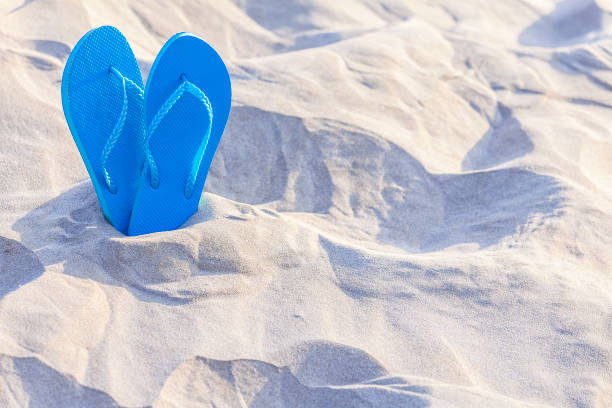 istock Pair of flip flops on white sand with copy space 1153701715
