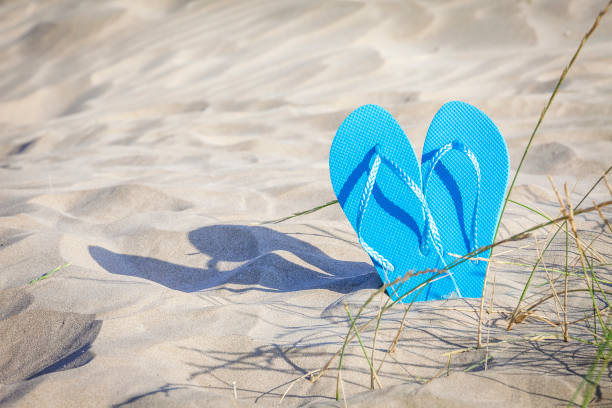 istock Pair of flip flops on white sand with copy space 1153701723
