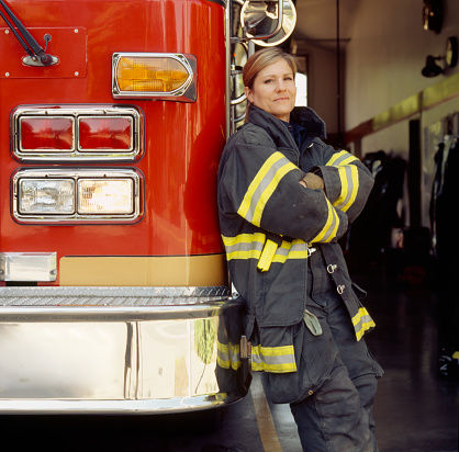 Smiling female woman firefighter with fire engine truck at station. Confident, successful public service career professional.