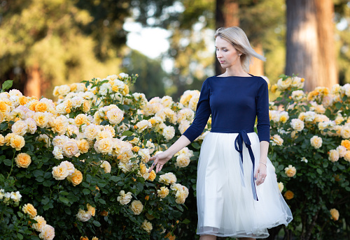 Young Caucasian woman walking in a rose garden near yellow roses.