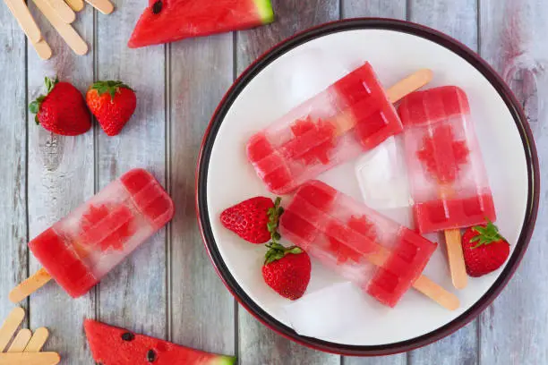Canadian flag popsicles, above view on a rustic wood table. Canada Day food concept.