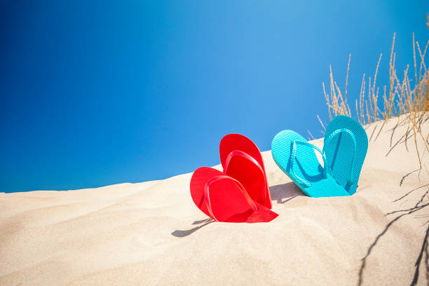 istock Two pairs of flip flops on white sand against blue sky with copy space 1153706620