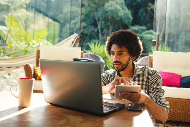 istock Young man using laptop and tablet in the living room 1153711760